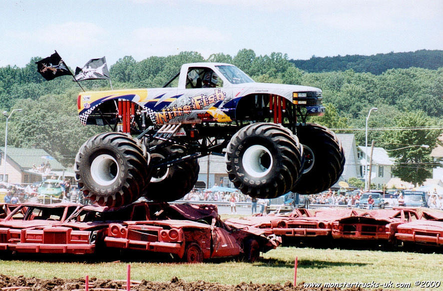 Nitrofish Monster Truck flying a low aerial assault over crushed cars