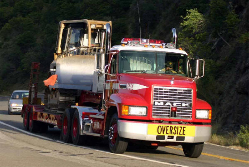 Picture of Mack Flatbed Truck hauling Caterpillar bulldozer oversize load. Heavy equipment mover- built like a mack truck